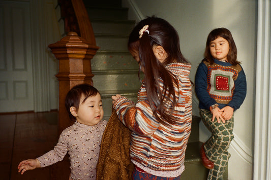 Three children interacting indoors by a staircase.